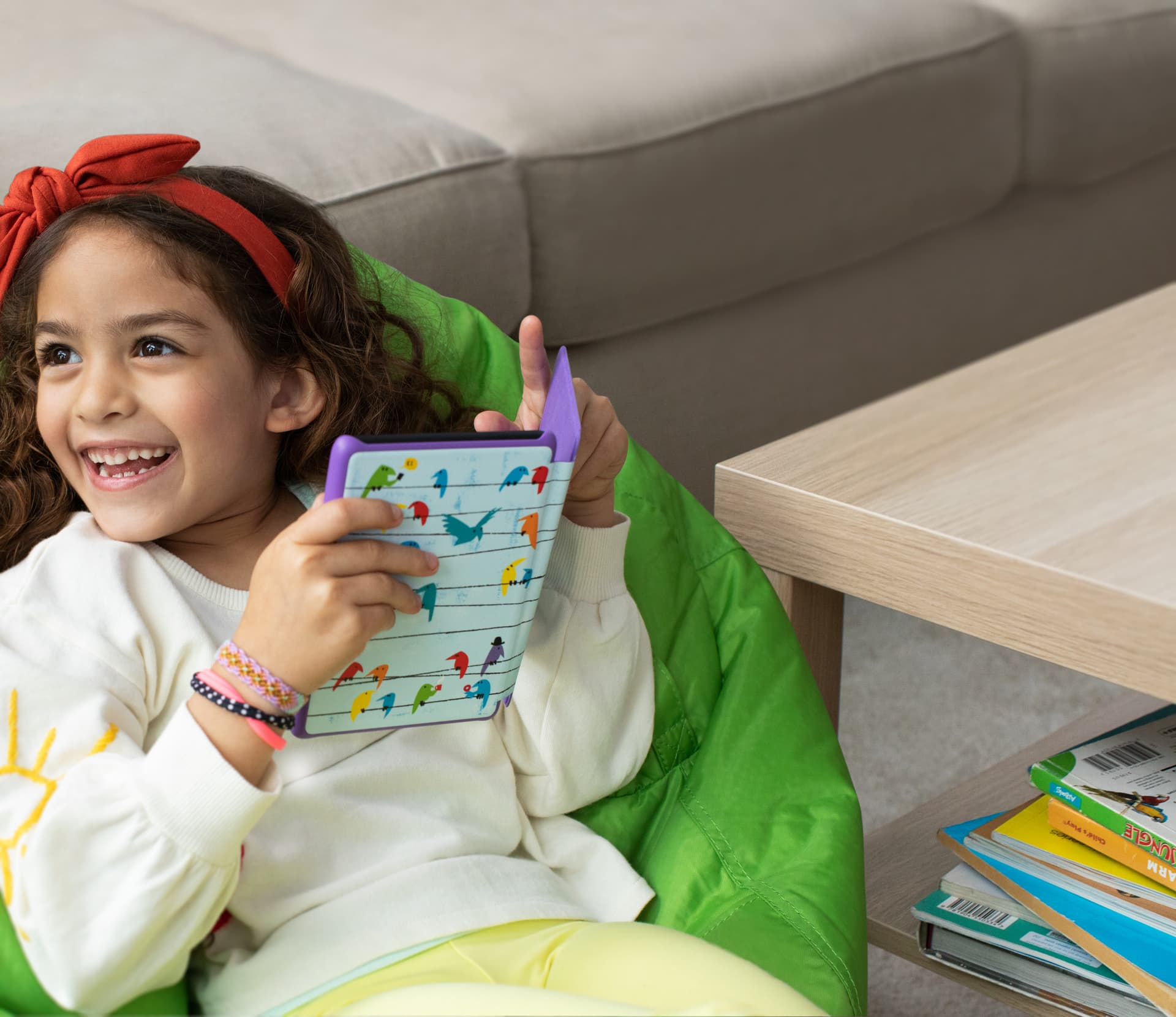 Young girl smiling and holding a purple illustrated Kindle Kids case in a living room
